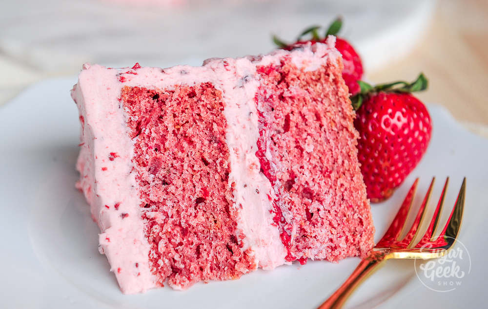 Strawberry cake on a dish next to a strawberry and fork