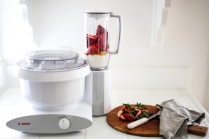 Bosch Universal Plus White Mixer with Blender Attachment on kitchen counter next to strawberries making a smoothie