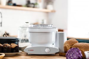 Bosch stand mixer on kitchen counter with bread and flour in the background.