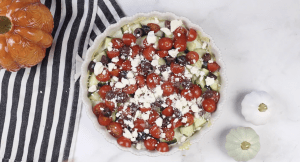 6 Layer Mediterranean Dip in a dish on a counter. Dip has hummus, tomatoes, cheese olives, sauces and cucumbers.